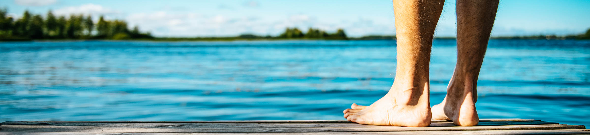 Beine und Füße eines Mannes auf einem Steg am See